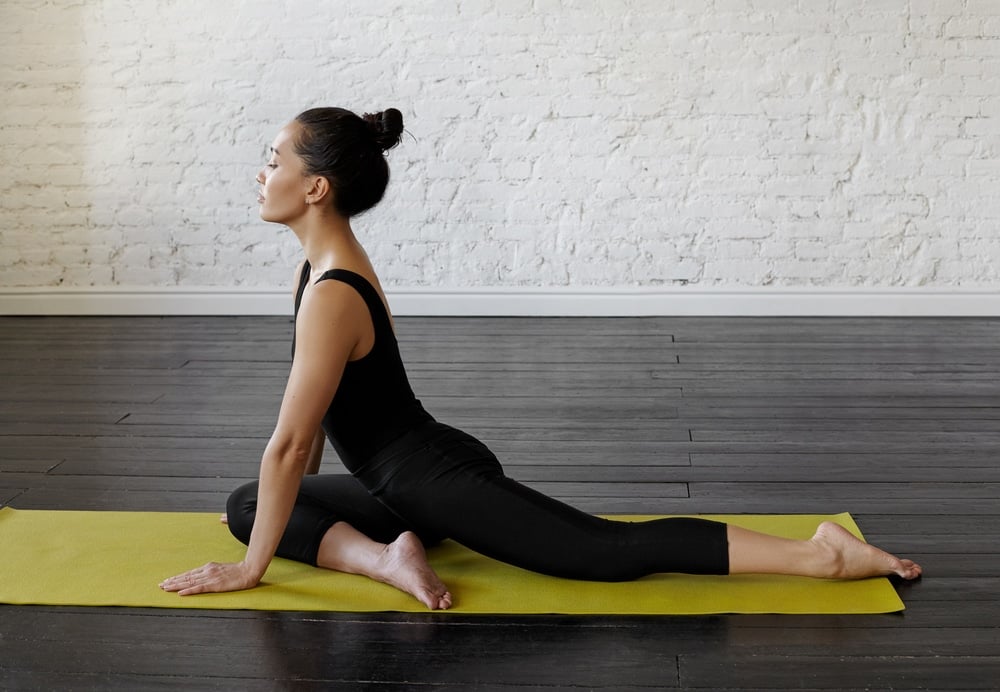 Woman doing a yoga pigeon pose on a yellow yoga mat.